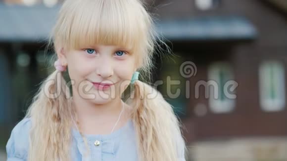 一个6岁的金发女孩的肖像对着镜头微笑它站在他房子的背景上带视频的视频的预览图