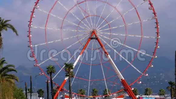 摩天轮在度假小镇棕榈树附近的云层映衬着蓝天阳光明媚视频的预览图