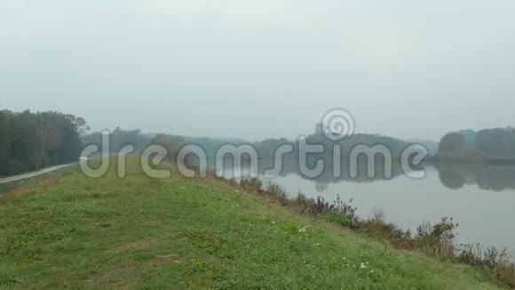 一架无人驾驶飞机在一座长满青草的小山上射击俯瞰一个雾蒙蒙的秋晨上清澈的反光湖视频的预览图