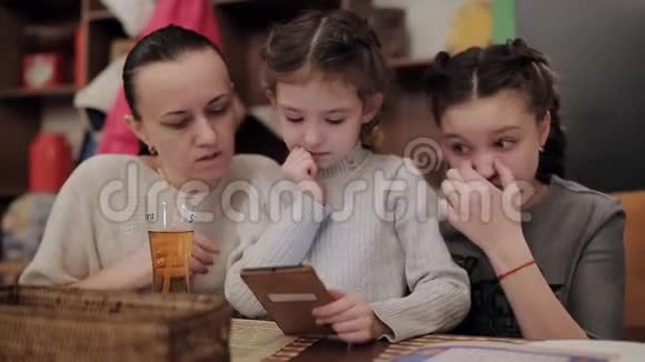 漂亮的妈妈和两个女儿在咖啡馆里用电话笑视频的预览图