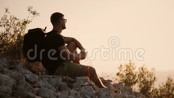 日落时分一个背着大背包的人正坐在山上视频的预览图
