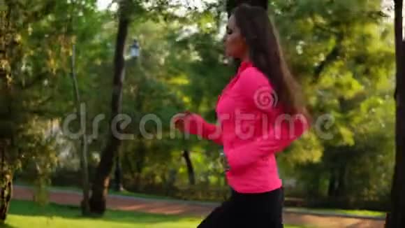 年轻女子穿着鲜艳的粉红色夹克在阳光明媚的城市公园里户外运动稳定射击视频的预览图