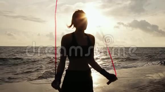 一位年轻女子在海滩边的一条斜斜的跳绳上慢动作地工作一个女孩在跳视频的预览图