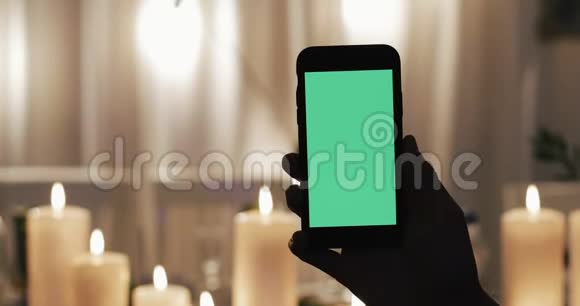男性手拿着绿色屏幕的智能手机在背景中点燃蜡烛视频的预览图