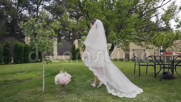 美丽的金发新娘穿着豪华的长婚纱在绿色的花园里散步新娘的早晨结婚日视频的预览图