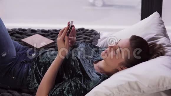 年轻女性靠窗在床上使用智能手机视频的预览图