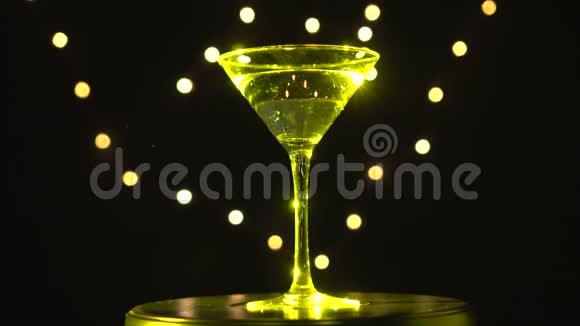 明亮的黄色鸡尾酒在玻璃旋转在黑暗的背景与模糊的光视频的预览图