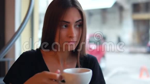 一个迷人的年轻女人坐在咖啡店的窗户旁用一杯热咖啡做梦休息视频的预览图