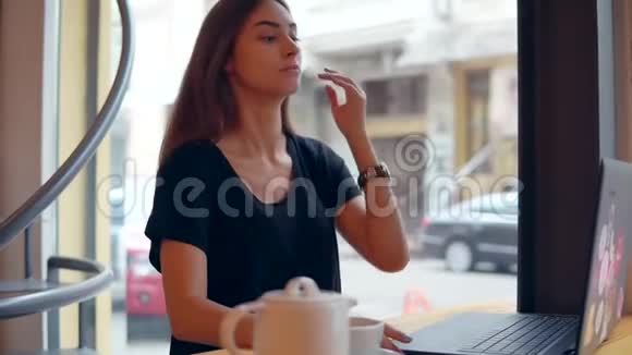年轻女子坐在窗边的咖啡店里休息一下她正在使用她的笔记本电脑工作和冲浪视频的预览图