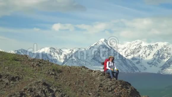 旅行者坐在山顶的女人从热水瓶里喝热茶红色背包橙色夹克草帽筷子视频的预览图