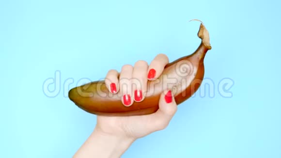 红色指甲的雌性手在蓝色背景上抓着一根红色的香蕉视频的预览图