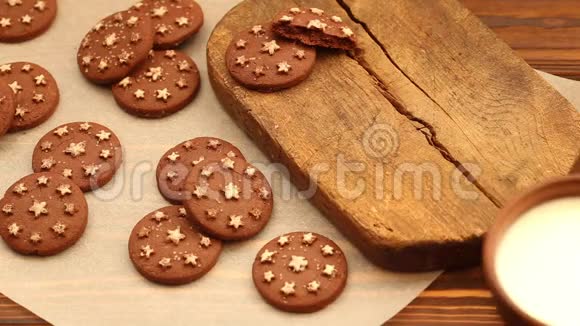 在旧木砧板上的粘土杯中放入热牛奶在羊皮纸上放入新鲜的烤巧克力饼干视频的预览图