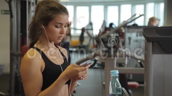 戴着耳机的年轻女子在室内健身房里站着电话视频的预览图