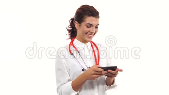 一位年轻微笑的护士用智能手机短信的肖像拥有听诊器的年轻医学专业人员视频的预览图