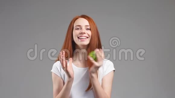 美丽的红头发女孩手里拿着一个绿色的苹果在白色的背景上微笑慢动作视频的预览图