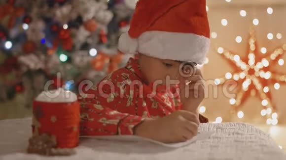 穿着睡衣戴着圣诞帽的梦男孩用棉花糖和一杯可可给圣诞老人写信视频的预览图