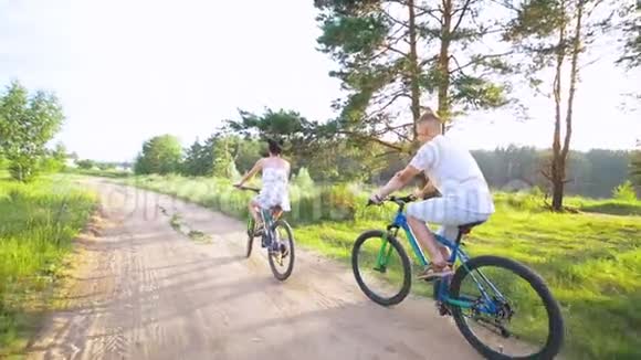 年轻快乐的一对在夏天的田野里骑自行车视频的预览图