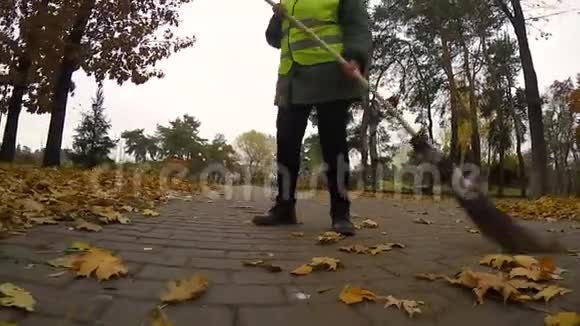 女看门人在秋天从树叶中清理公园这是最辛苦最低收入的工作视频的预览图