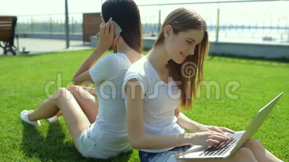 两个漂亮的女孩在草地上背靠背坐在一起视频的预览图