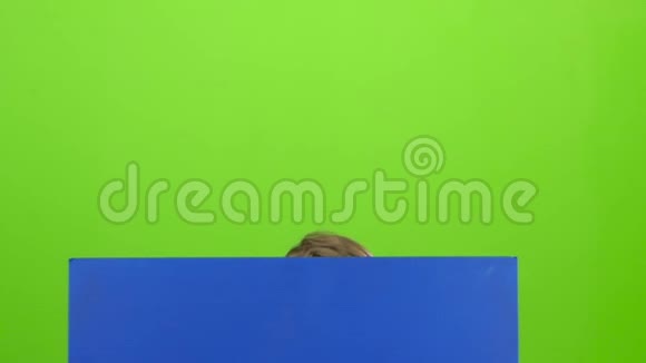 小男孩从蓝色海报后面看出来在绿色屏幕前挥动一只手慢动作视频的预览图