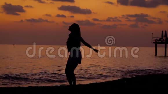 幸福苗条的女人在日落后的傍晚在海边跳跃双手腾空而起视频的预览图