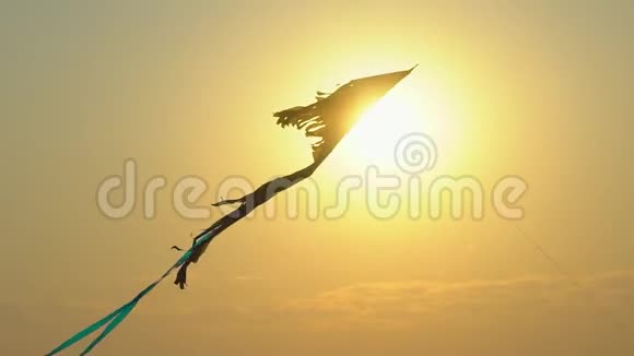 特写玩具风筝在风中高高飘扬映衬金色晚霞天空背景太阳镜头耀斑五颜六色的风筝飞进来视频的预览图