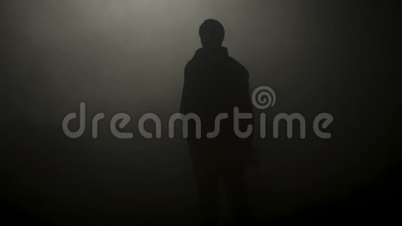 黑色轮廓的人站在烟雾弥漫的黑暗中库存录像年轻男子神秘的轮廓在黑暗中闪耀视频的预览图