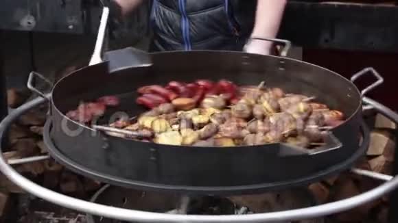 一个男人在一个大圆烤架上准备香肠和蔬菜视频的预览图