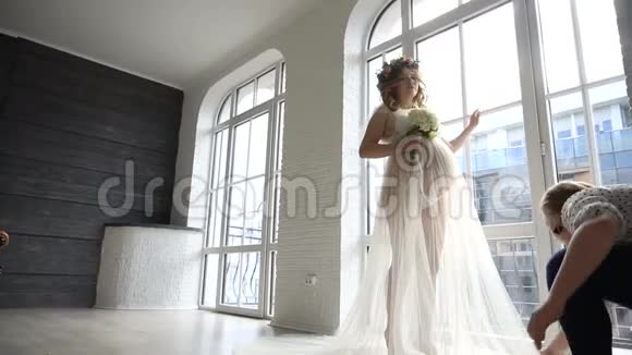 女助理协助在工作室为怀孕的新娘穿上婚纱视频的预览图