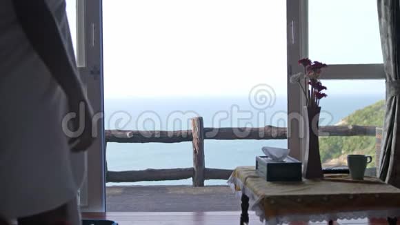 美丽的女孩走向海景露台醒来双手伸展从阳台眺望海景地平线视频的预览图
