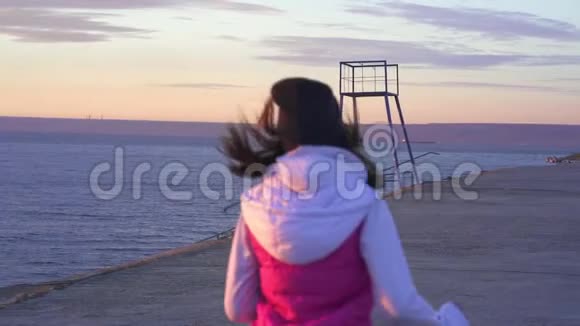 下面的动作年轻苗条的女孩戴着运动帽和运动衫早上在大河堤上慢跑视频的预览图