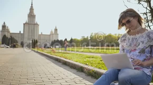 在莫斯科国立大学背景的广场上一个手持笔记本电脑的金发女学生视频的预览图