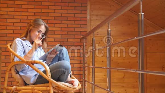 小女孩在家里用平板电脑坐在柳条椅上视频的预览图