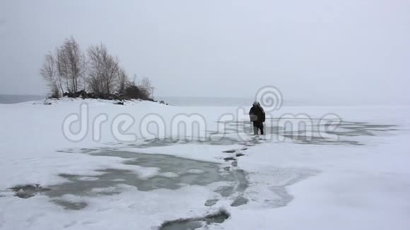 背着背包的人在融化的河面上的暴风雪中行走视频的预览图