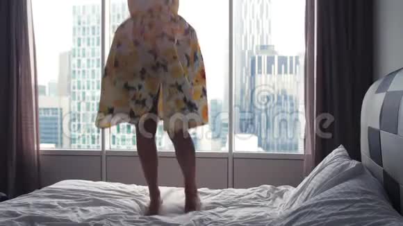 穿着连衣裙的年轻快乐女子跳上酒店的床慢动作3840x2160视频的预览图