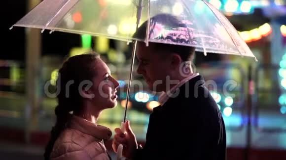 年轻漂亮的夫妇晚上一起在游乐园约会雨天秋天站着的情人视频的预览图