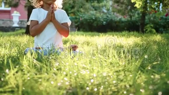 小可爱的女婴在绿色的夏天公园里草地上冥想视频的预览图