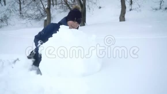 男孩在冬天为雪人滚动大雪球视频的预览图