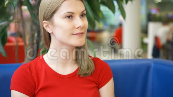 一幅美丽梦幻的年轻女子穿着红色t恤坐在咖啡馆里思考的肖像蓝沙发青树视频的预览图