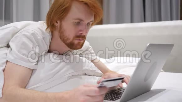 网上购物红发胡子男在床上笔记本电脑支付视频的预览图