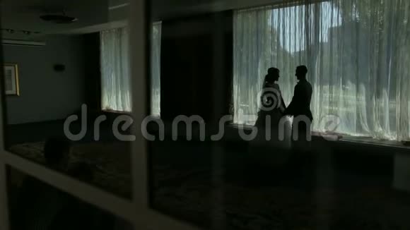新婚夫妇的剪影靠近窗户视频的预览图