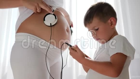 手里拿着手机的小男孩把耳机放在孕妇肚子上视频的预览图