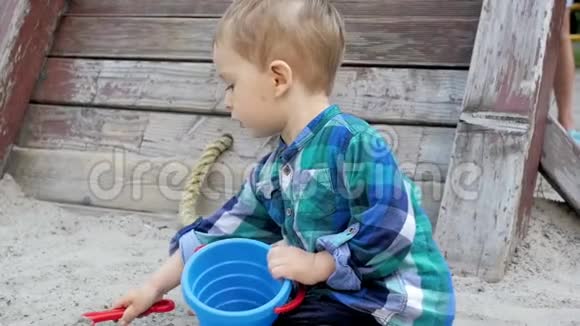 在公园里用塑料玩具铲子挖沙子的可爱金发幼儿男孩慢镜头视频的预览图