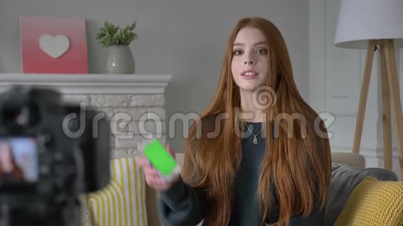 年轻的红发女孩博客写手微笑着对着镜头说话显示出新的购买智能手机应用程序绿色视频的预览图