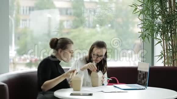 两个戴眼镜的漂亮女人一边吃筷子一边做紧急的生意视频的预览图