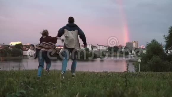 夕阳西下年轻幸福的夫妇在河岸上奔跑男人和女人在一起玩得很开心视频的预览图