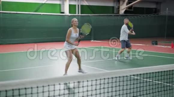 快乐夫妻在室内球场打网球的形象穿着运动服装的年轻人在一起视频的预览图