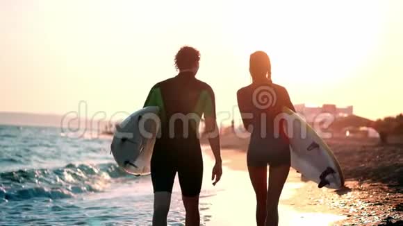 慢动作一对年轻的男女冲浪者穿着湿衣服在海滩上散步手中握着视频的预览图