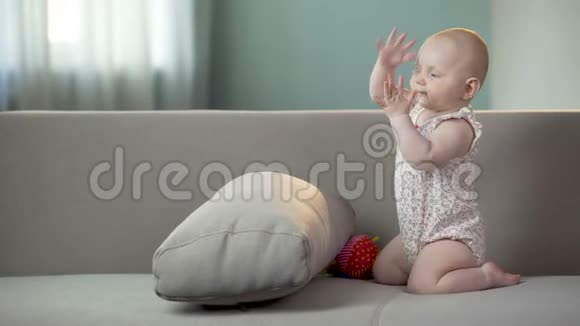 积极主动的女婴在家里的沙发上拍手和玩耍童年快乐视频的预览图