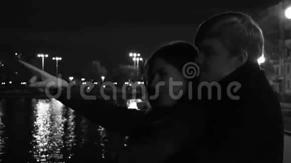 一对相爱的情侣站在海滨城市的灯光下晚上在河边的一对新婚夫妇视频的预览图